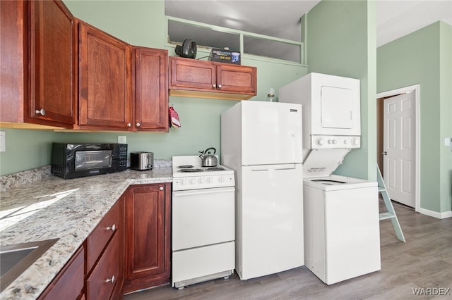 kitchen with white appliances, light stone counters, light wood finished floors, a sink, and stacked washer and clothes dryer