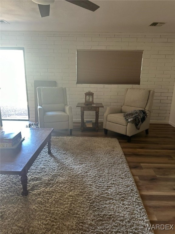 living area with visible vents, dark wood finished floors, and brick wall