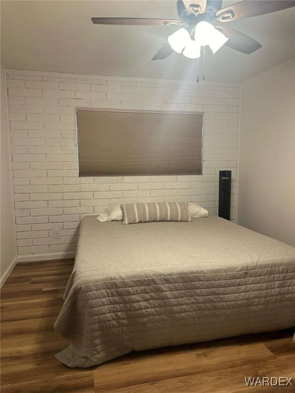 bedroom featuring a ceiling fan, baseboards, brick wall, and wood finished floors