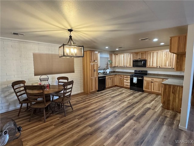 kitchen featuring dark wood-style flooring, a sink, hanging light fixtures, and black appliances