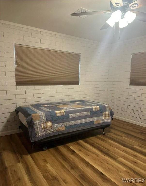 bedroom featuring dark wood-style floors, brick wall, and a ceiling fan