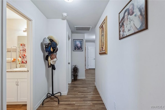 hall featuring dark wood finished floors, visible vents, attic access, a sink, and baseboards