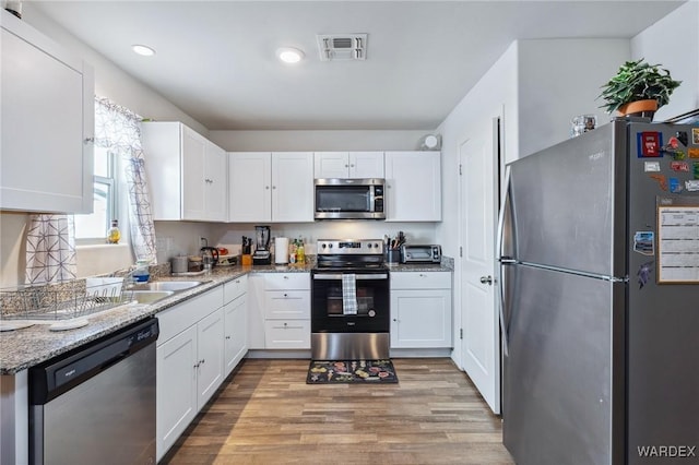 kitchen featuring stainless steel appliances, visible vents, white cabinets, light stone countertops, and light wood finished floors