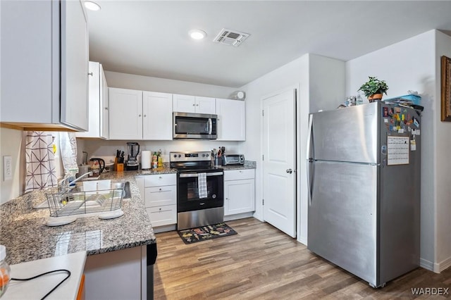 kitchen with visible vents, appliances with stainless steel finishes, light wood-type flooring, stone counters, and white cabinetry