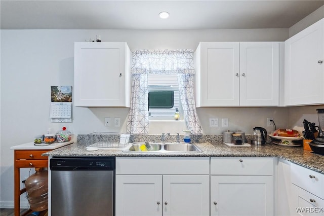 kitchen featuring stainless steel dishwasher, dark stone countertops, a sink, and white cabinets