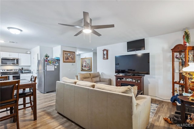 living area with a toaster, a fireplace, a ceiling fan, visible vents, and light wood-style floors