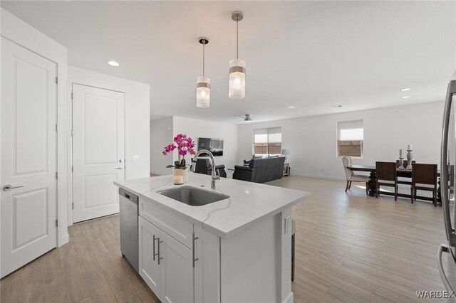 kitchen featuring a center island with sink, dishwasher, light stone counters, hanging light fixtures, and a sink