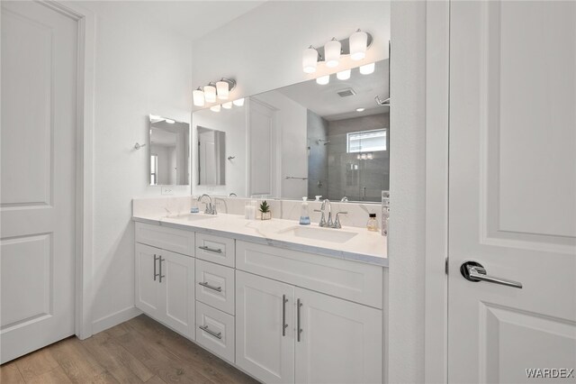 full bathroom featuring double vanity, a sink, a shower stall, and wood finished floors