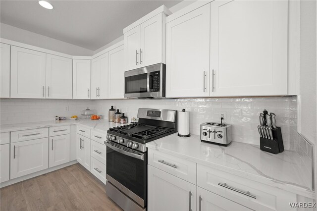 kitchen with light stone counters, light wood-style flooring, white cabinetry, appliances with stainless steel finishes, and decorative backsplash