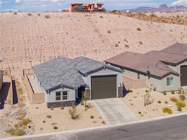 view of front of home with concrete driveway, stone siding, an attached garage, a mountain view, and stucco siding