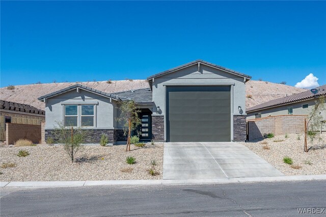 view of front of home with concrete driveway, stone siding, an attached garage, fence, and stucco siding