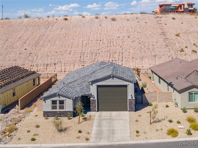 view of front facade featuring stucco siding, concrete driveway, an attached garage, fence, and stone siding