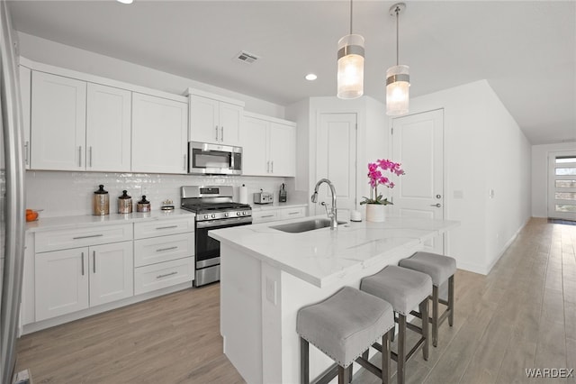 kitchen with white cabinetry, stainless steel appliances, a sink, and decorative light fixtures