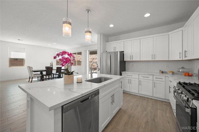 kitchen with white cabinets, hanging light fixtures, a kitchen island with sink, stainless steel appliances, and a sink