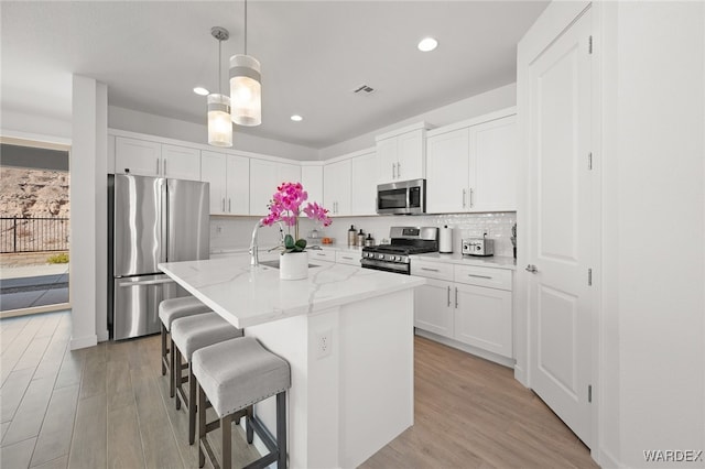 kitchen featuring visible vents, appliances with stainless steel finishes, white cabinets, an island with sink, and light stone countertops