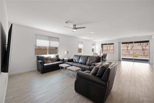 living room featuring light wood finished floors, a ceiling fan, visible vents, and baseboards