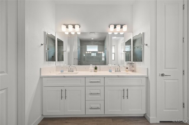 bathroom featuring wood finished floors, a sink, a shower stall, and double vanity