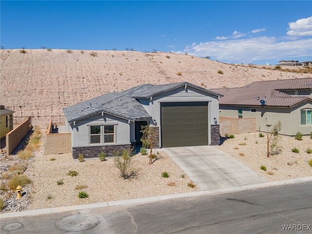 view of front of house featuring an attached garage, fence, stone siding, driveway, and stucco siding