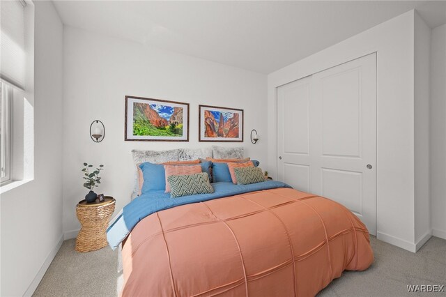 bedroom with a closet, light colored carpet, and baseboards