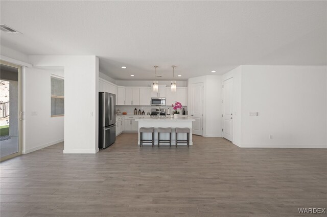 kitchen featuring stainless steel appliances, white cabinetry, hanging light fixtures, light countertops, and a center island with sink