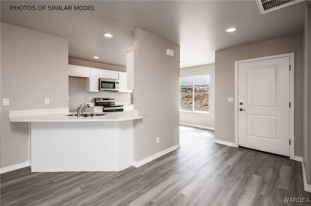 kitchen featuring wood finished floors, a sink, white cabinets, light countertops, and appliances with stainless steel finishes