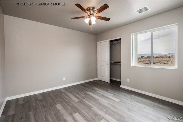 unfurnished bedroom featuring a closet, wood finished floors, visible vents, ceiling fan, and baseboards