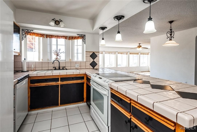 kitchen featuring decorative light fixtures, light tile patterned floors, tile counters, a sink, and white appliances