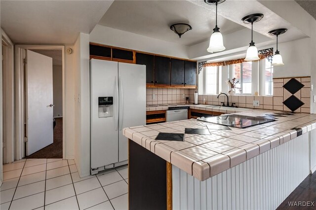 kitchen with white refrigerator with ice dispenser, dishwasher, tile countertops, a peninsula, and pendant lighting