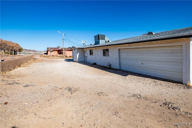 exterior space featuring a garage, dirt driveway, fence, and cooling unit