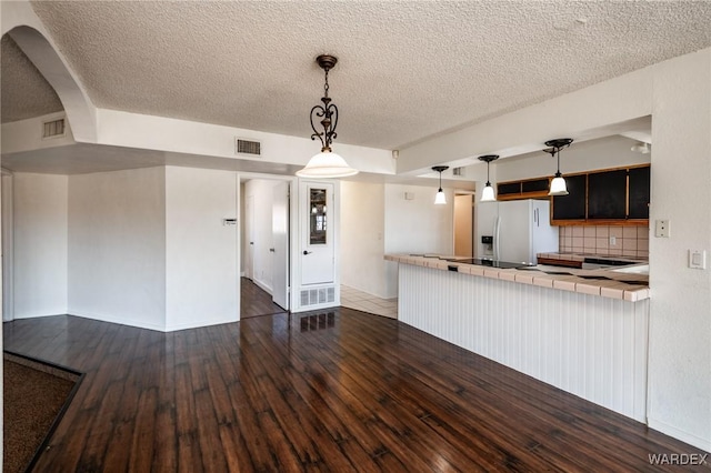 kitchen featuring hanging light fixtures, visible vents, dark wood-style flooring, and stainless steel fridge with ice dispenser