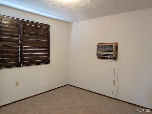 unfurnished room with a wall mounted air conditioner, baseboards, and a textured ceiling