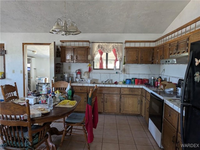 kitchen with tile counters, white electric stove, under cabinet range hood, an inviting chandelier, and freestanding refrigerator
