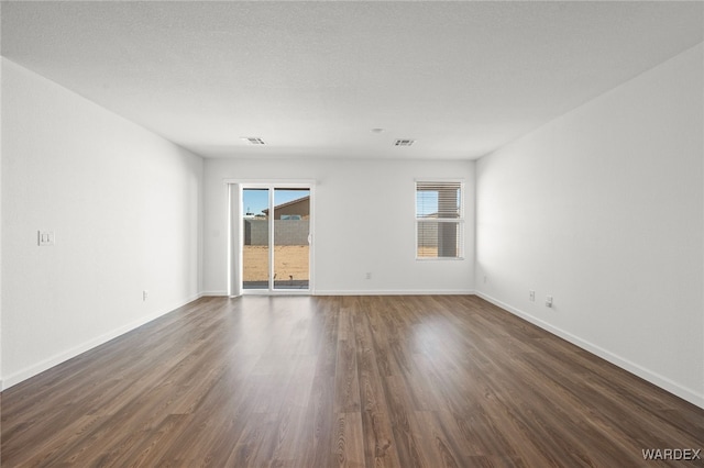 spare room featuring dark wood-type flooring, visible vents, and baseboards