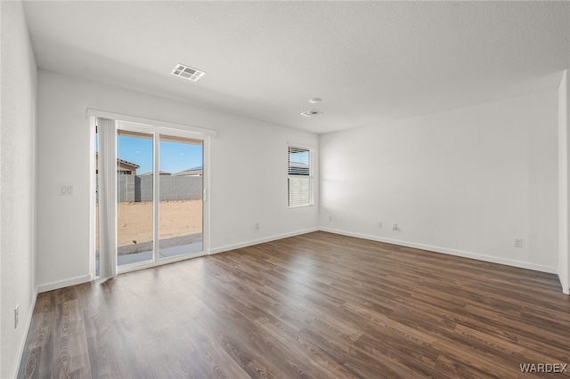 spare room with baseboards, a textured ceiling, visible vents, and dark wood-type flooring