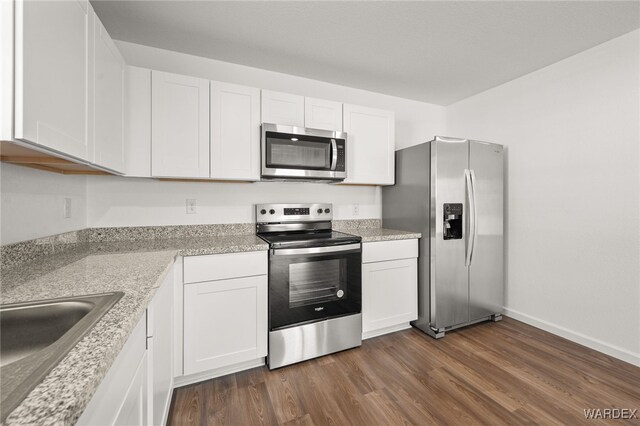 kitchen with dark wood-style floors, appliances with stainless steel finishes, white cabinetry, a sink, and baseboards