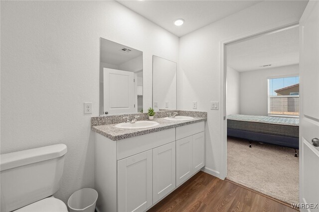 ensuite bathroom featuring a sink, ensuite bath, toilet, and wood finished floors