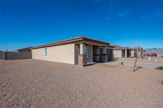 exterior space featuring stucco siding, fence, a garage, driveway, and a tiled roof