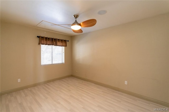 spare room featuring light wood-type flooring, attic access, and baseboards