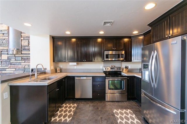 kitchen featuring dark brown cabinets, appliances with stainless steel finishes, dark tile patterned floors, and a sink