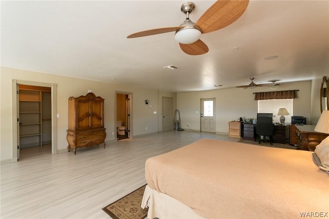 bedroom with visible vents, baseboards, ceiling fan, a walk in closet, and light wood-style floors