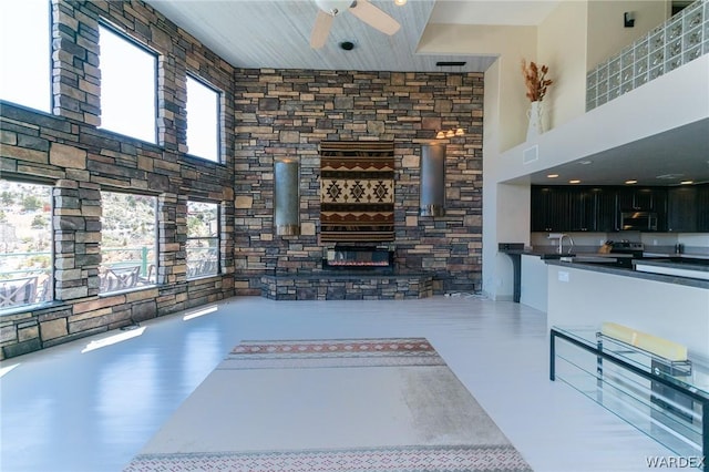 unfurnished living room with ceiling fan, a high ceiling, a sink, visible vents, and a glass covered fireplace