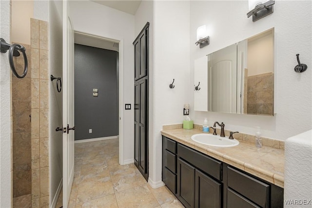 full bath with a tile shower and vanity