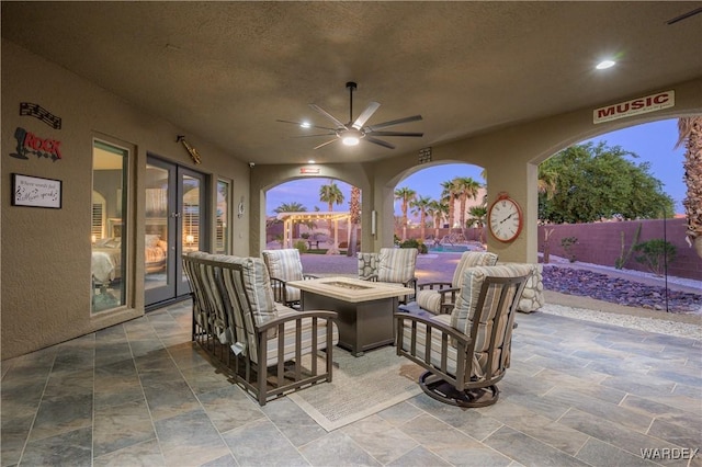 patio terrace at dusk featuring an outdoor fire pit, fence, and a ceiling fan