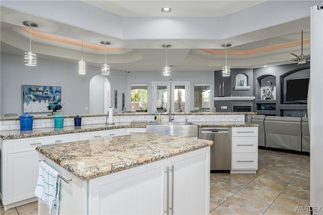 kitchen featuring a tray ceiling, open floor plan, hanging light fixtures, and stainless steel dishwasher