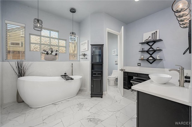 full bath with a freestanding tub, marble finish floor, toilet, and vanity