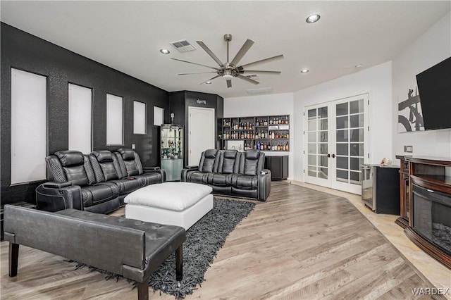 living area featuring visible vents, a glass covered fireplace, light wood-type flooring, french doors, and a bar