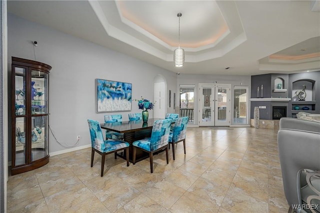 dining area featuring baseboards, a raised ceiling, arched walkways, and a glass covered fireplace