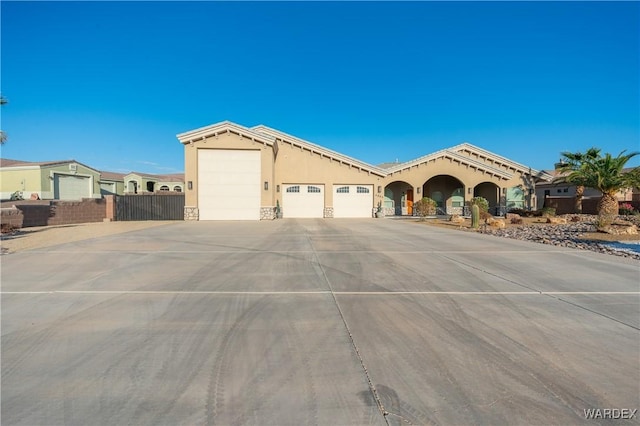 mediterranean / spanish-style home with an attached garage, fence, driveway, stone siding, and stucco siding