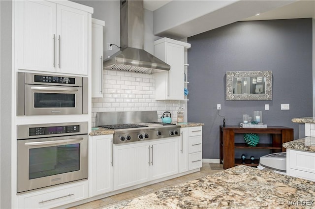 kitchen with light stone counters, backsplash, appliances with stainless steel finishes, white cabinets, and wall chimney exhaust hood