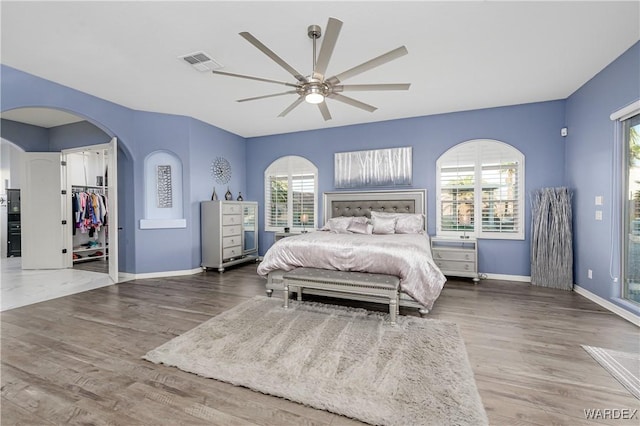 bedroom with arched walkways, wood finished floors, visible vents, and baseboards